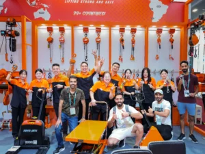 Tim Megajaya.co.id berfoto bersama pengunjung di booth pameran Canton Fair dengan latar display produk lifting equipment